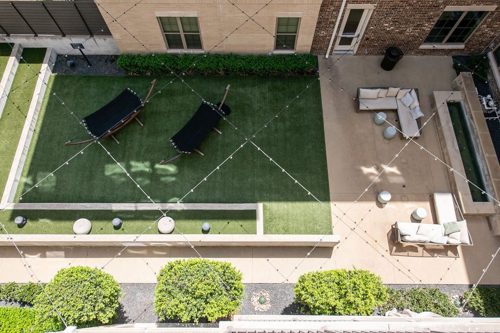 A patio with a table and chairs is surrounded by a green lawn and bushes.