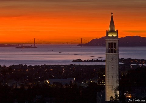 A cityscape with a prominent tower and a bridge in the background during sunset.