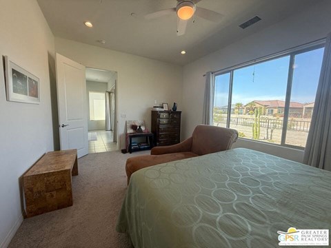 A bedroom with a large bed and a view of the backyard through the window.