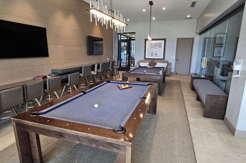 A pool table is in the middle of a room with a TV and a bench.