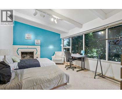 A bed with a grey and white patterned comforter sits in a bedroom with a white ceiling and a wooden floor.
