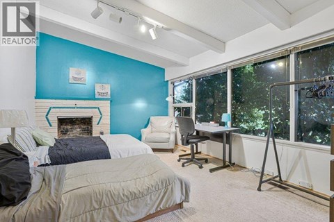 A bed with a grey and white patterned comforter sits in a bedroom with a white ceiling and a wooden floor.