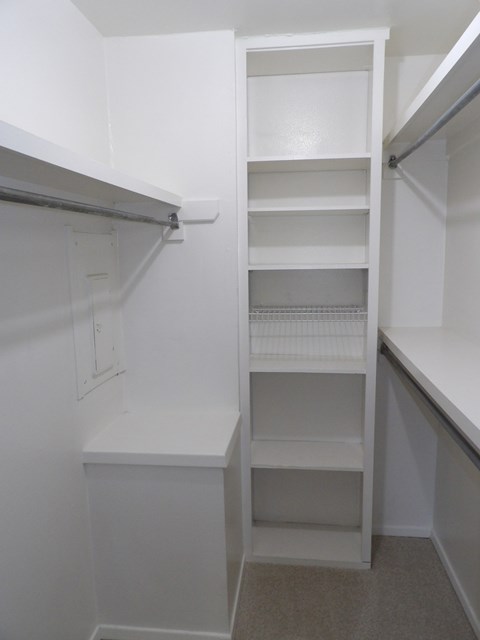 A white walk-in closet with shelves and a bench.