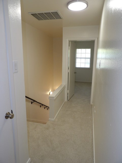 A hallway with a carpeted floor and a door on the left.