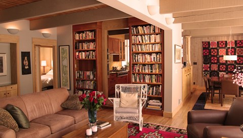 A living room with a brown couch, a white chair, and a bookshelf filled with books.