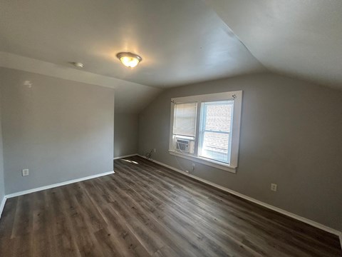 A room with wooden flooring and a window with blinds.