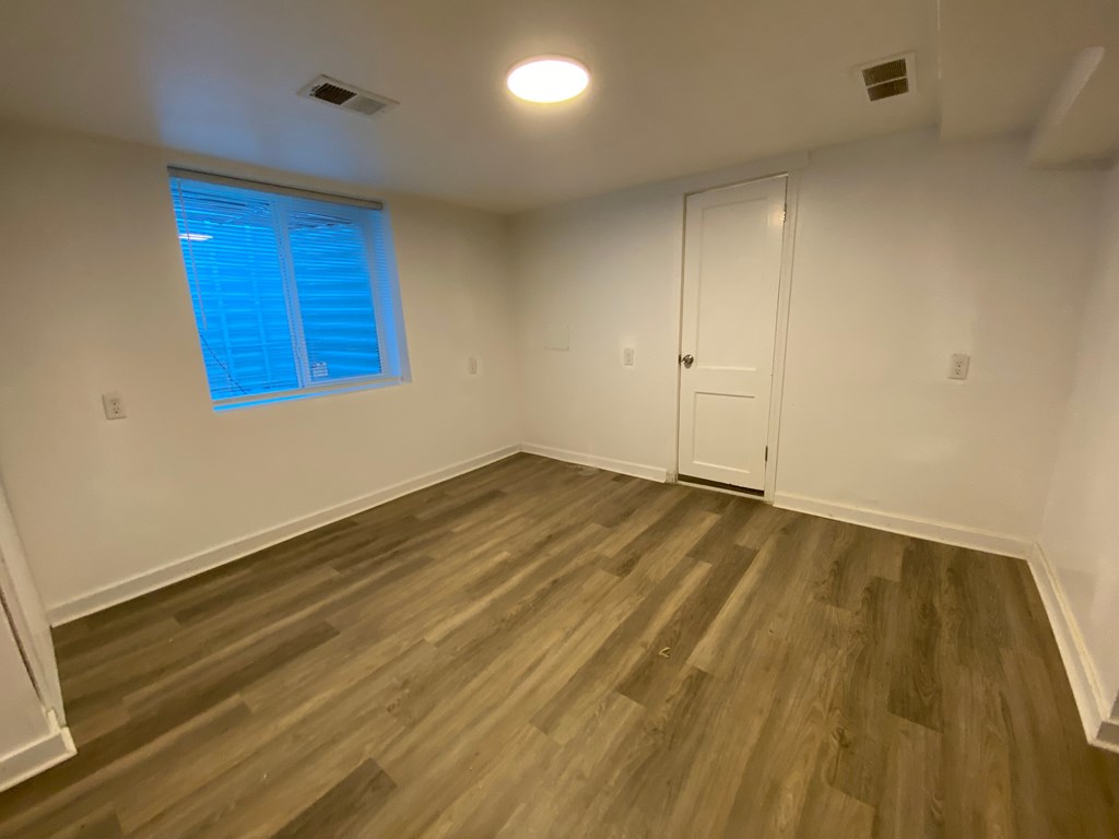 A room with wooden flooring and a window with blinds.