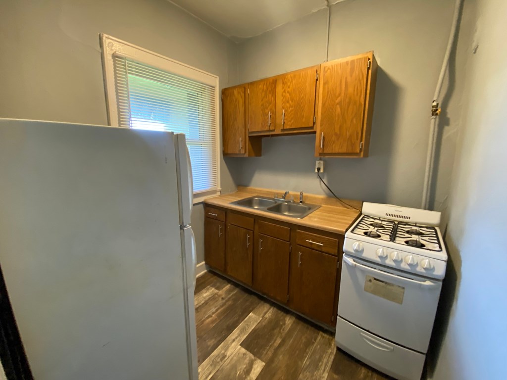 A small kitchen with a white fridge, wooden cabinets, and a white gas stove.