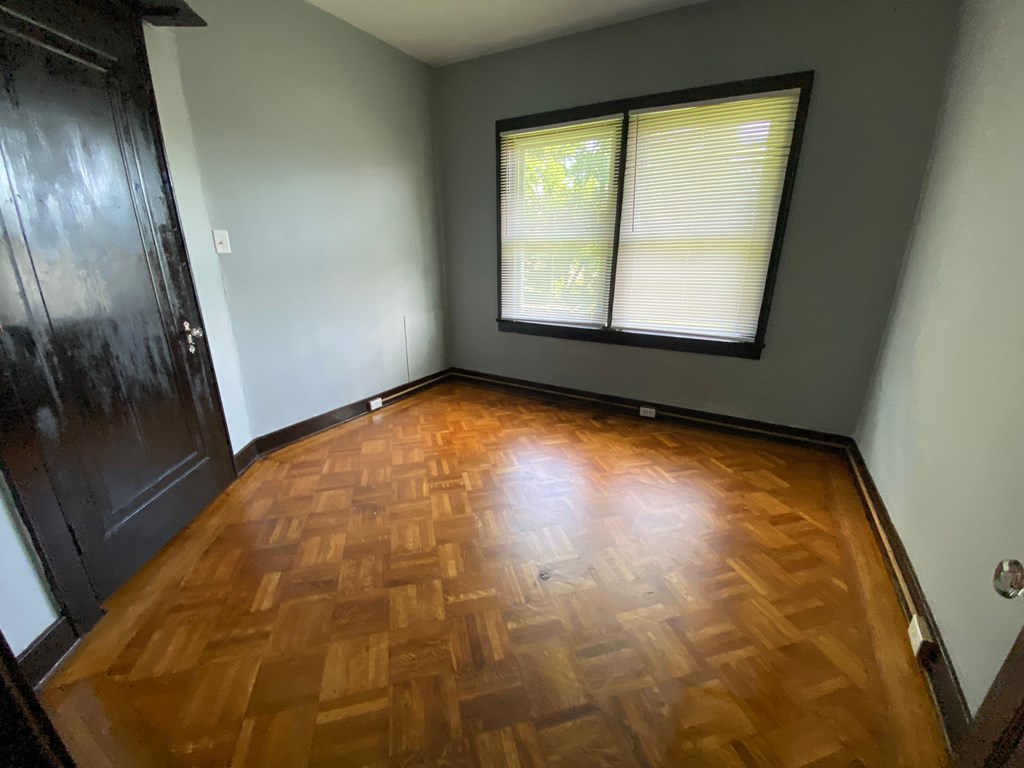 A room with a wooden floor and a window with blinds.