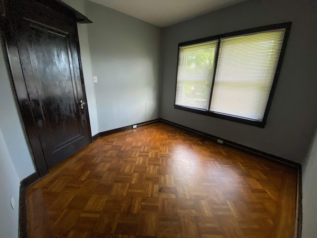 A room with a wooden floor and a window with blinds.