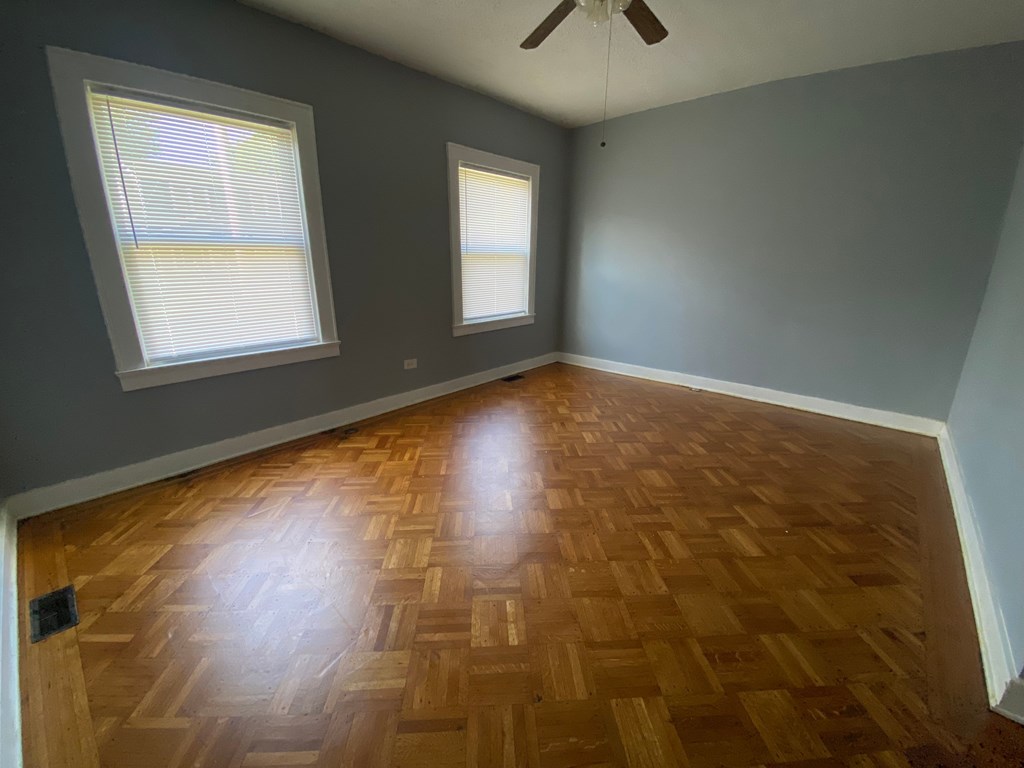 A room with wooden flooring and two windows.