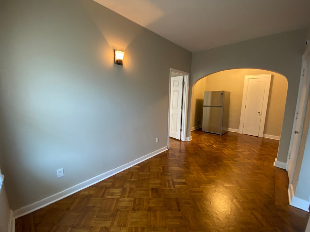 A room with wooden flooring and a refrigerator in the corner.