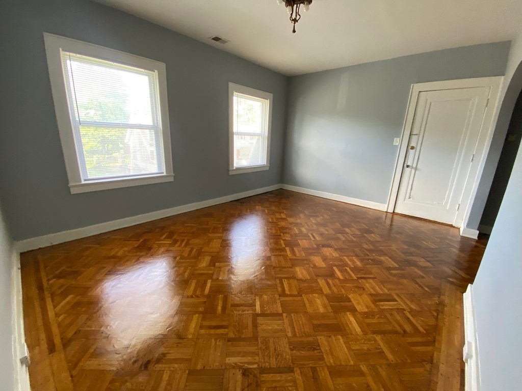 A room with wooden flooring and two windows.