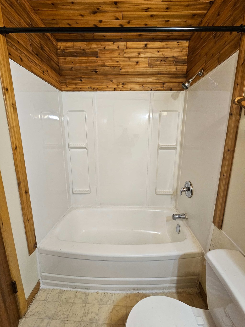 A white bathroom with wooden ceiling and a white tub.