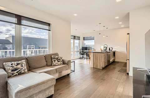 A modern living room with a large window and a kitchen area.