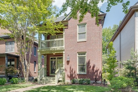 A red brick house with a white window and a green tree in front.