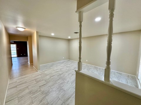 A spacious room with a wooden floor and a staircase with a white railing.