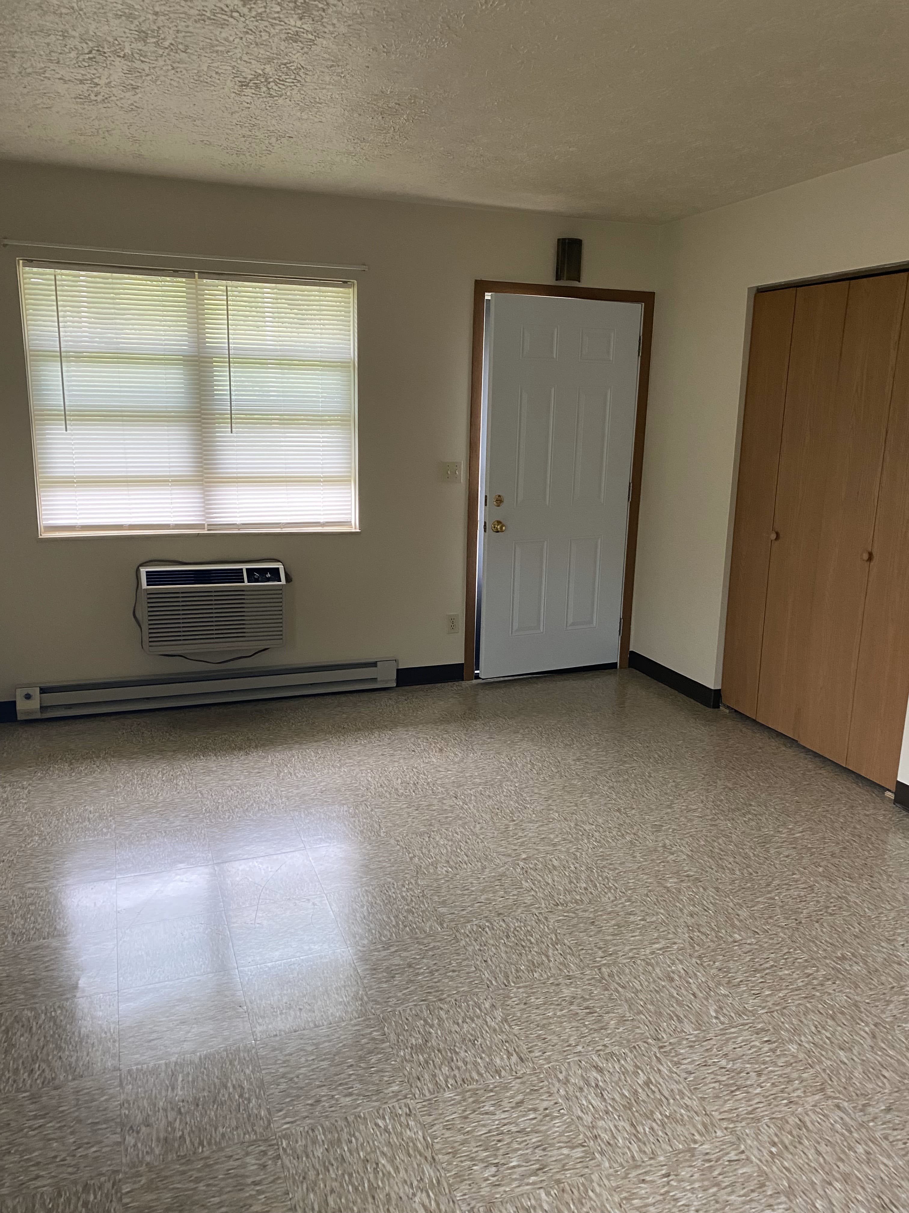 A room with a window, a door, and a wall-mounted air conditioner.