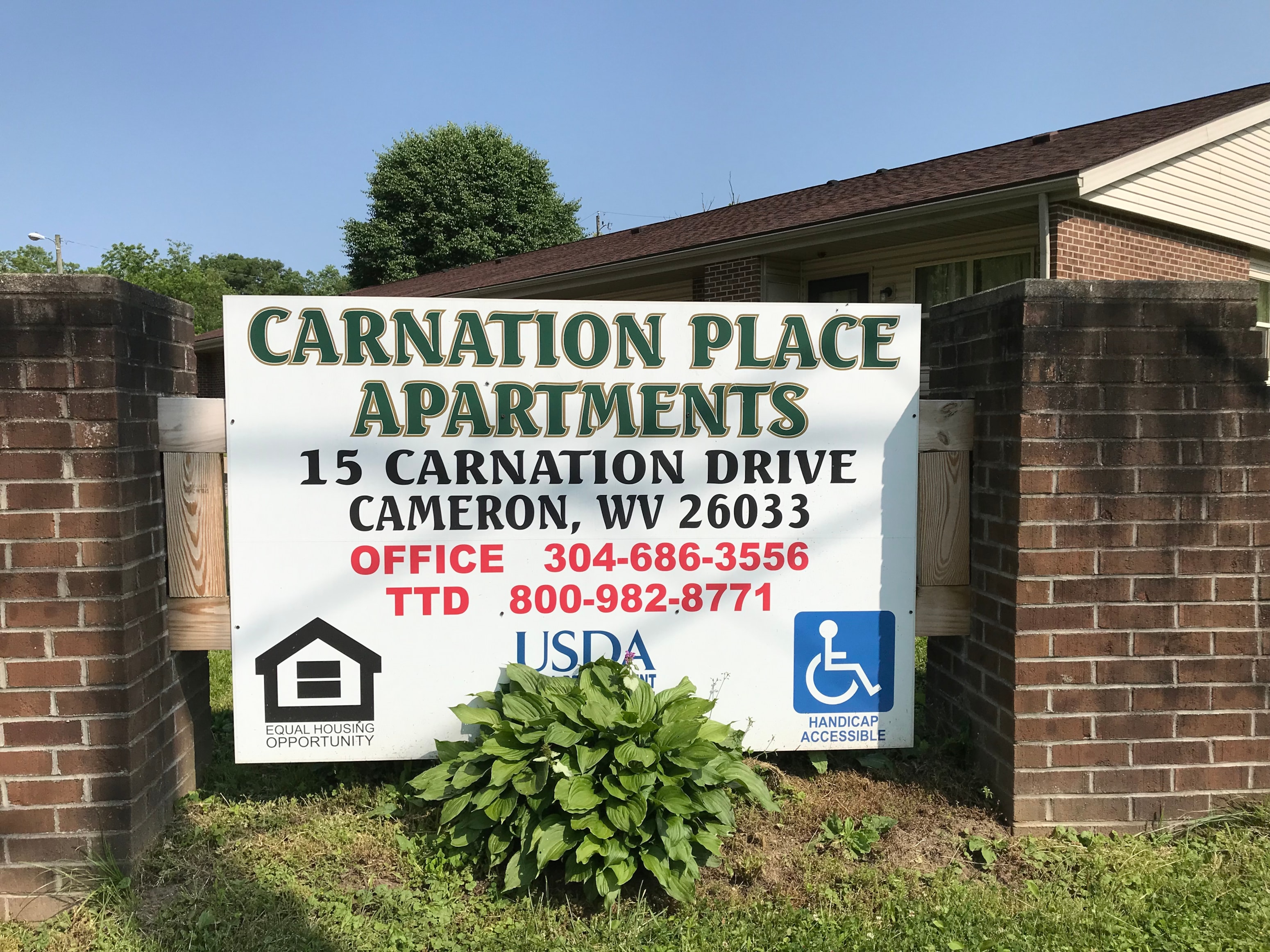 A sign for Carnation Place Apartments is displayed in front of a brick wall.