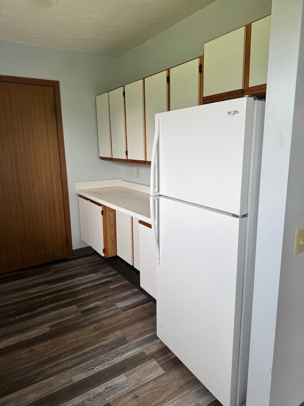 A white refrigerator in a kitchen with wooden cabinets.