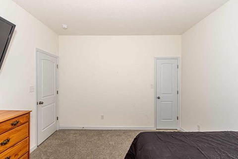 A bedroom with a bed, dresser, and two doors.