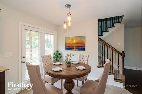 A dining room with a wooden table and chairs, a painting on the wall, and a staircase with a railing.