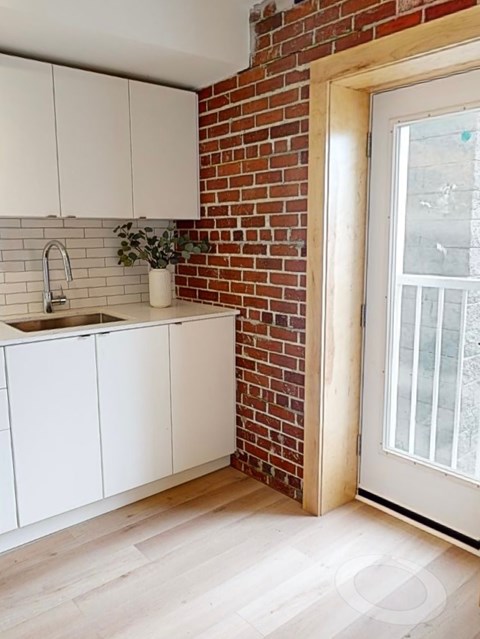 A kitchen with white cabinets and a brick wall.