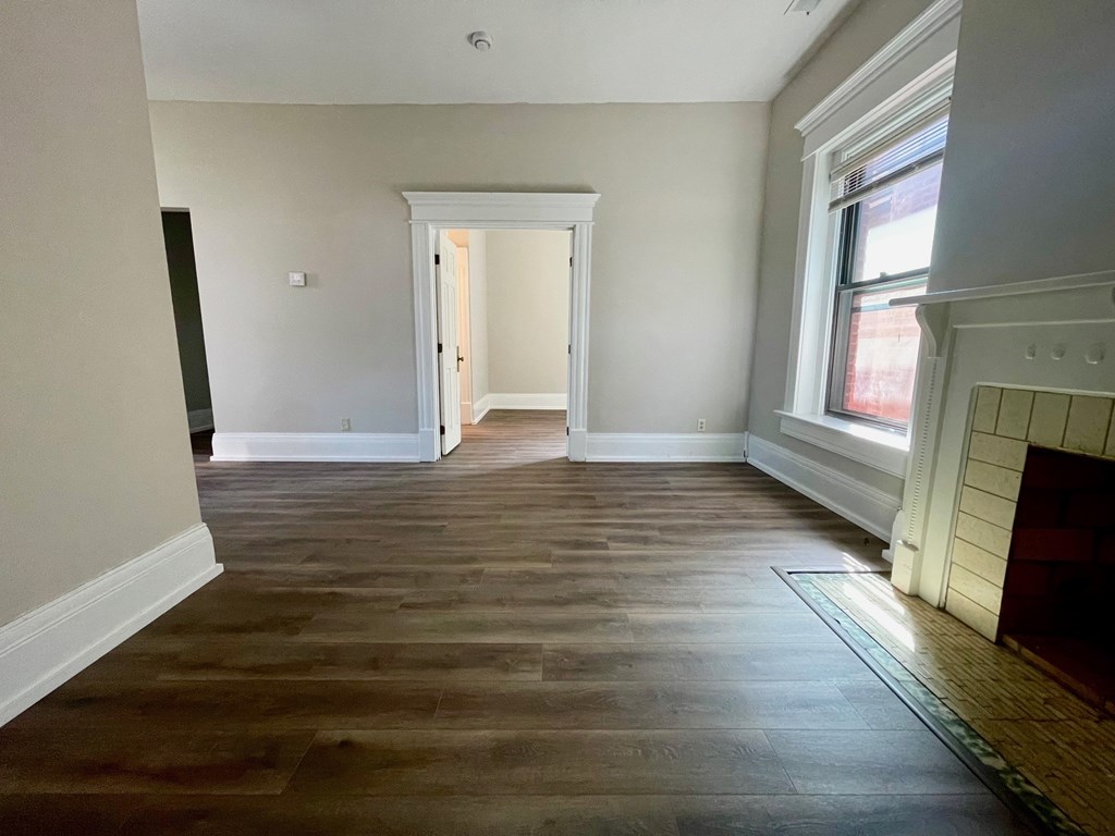 A room with wooden flooring and a fireplace on the right side.