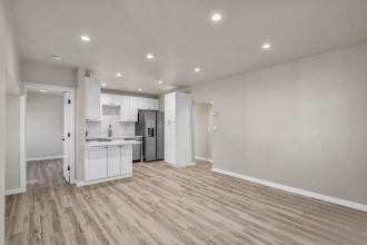 A kitchen with white cabinets and a refrigerator is visible through an open door.