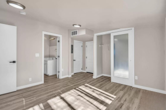 A room with white walls and wooden flooring with a white door on the left and a white wardrobe on the right.