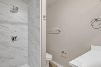 A white toilet sits in a bathroom with a marble tile shower.