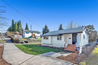 A white house with a brown door and a grey roof.