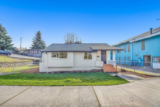 A white house with a grey roof is surrounded by a green lawn.