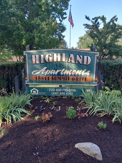 A sign for Highland Apartments is displayed in front of a hedge.