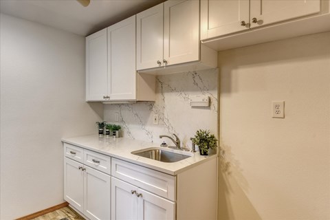 A kitchen with white cabinets and a marble backsplash.