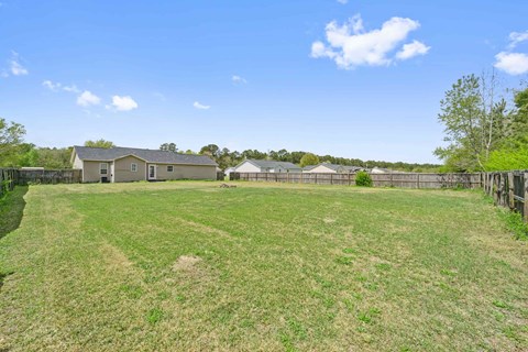 A large grassy field with a house and fence in the background.