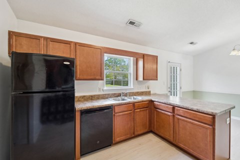 A black refrigerator is in a kitchen with wooden cabinets.