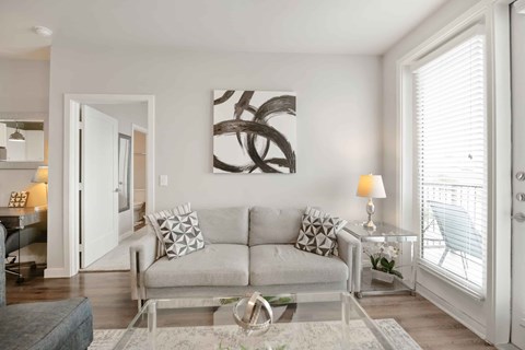 A modern living room with a grey couch and a large abstract painting on the wall.