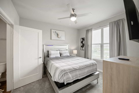 A bedroom with a bed, a ceiling fan, and a television.