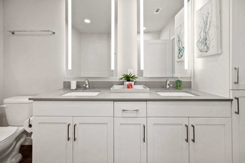 A white bathroom with a double sink vanity and a toilet.