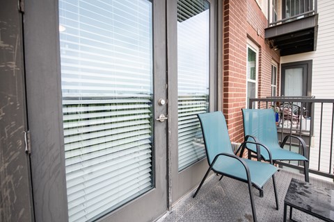 A balcony with a blue chair and a glass door.