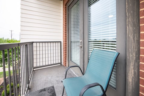 A blue chair sits on a balcony next to a window with blinds.
