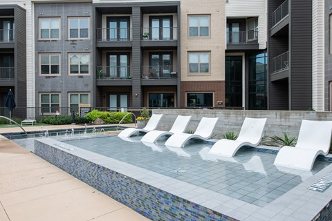 A pool with white chairs in front of apartment buildings.