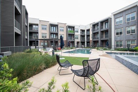 Two black chairs are on a concrete patio in front of apartment buildings.
