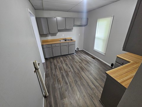 A kitchen with wood flooring and a window with blinds.