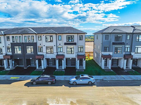 Two cars are parked in front of a row of townhouses.