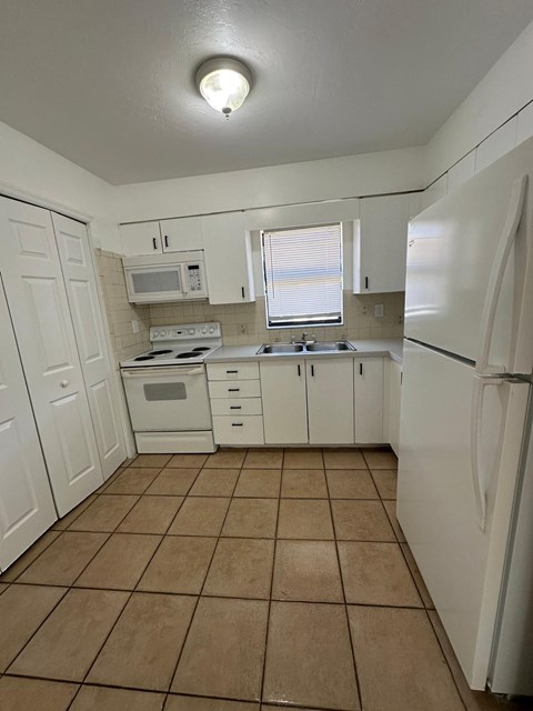 A kitchen with white appliances and brown tiles.
