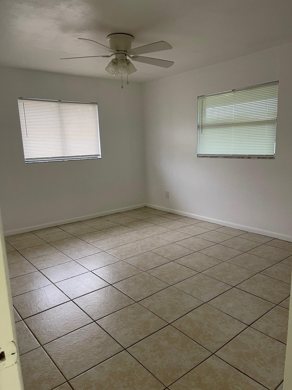 A room with a ceiling fan and two windows.