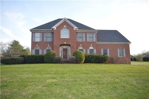 A red brick house with a black roof and a green lawn in front.