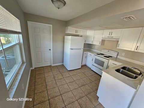 A kitchen with white appliances and beige tiles.